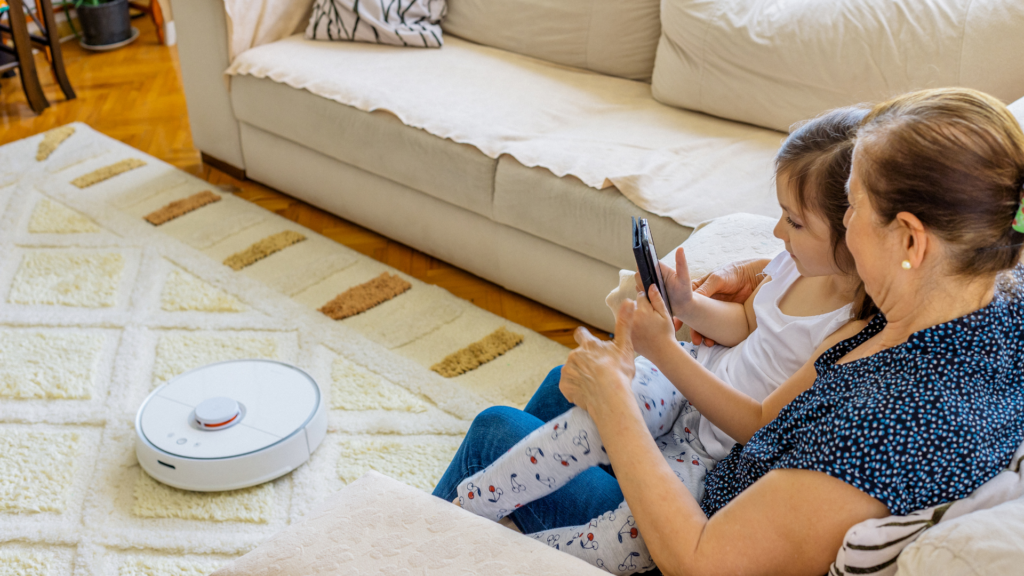 Robot vacuum cleaning the carpet while  woman and girl sitting on a couch looking at a cellphone
